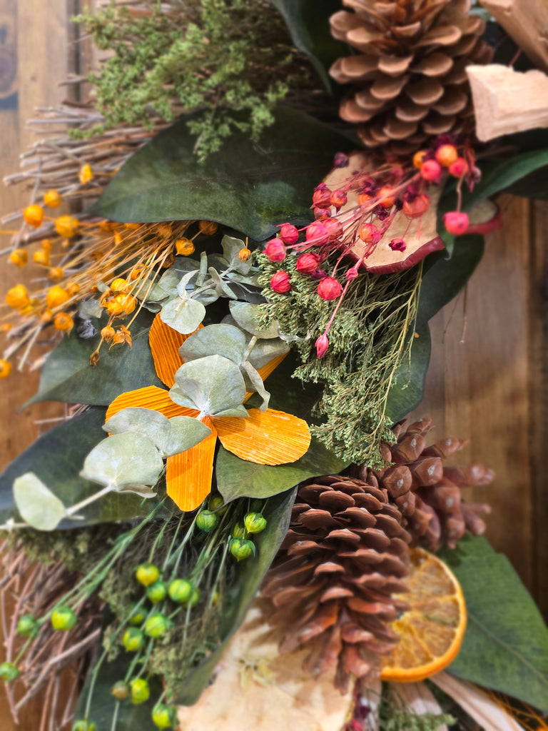 Decorative wreath with pine cones, berries, and greenery on a wooden surface