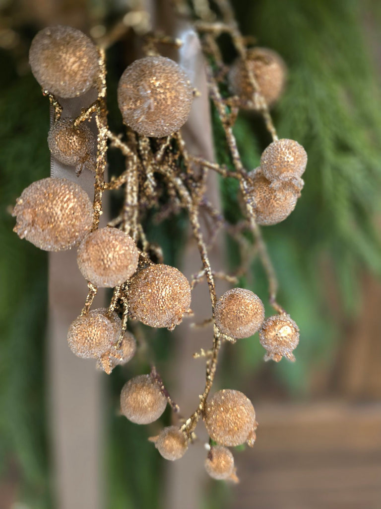 Decorative gold berries on a branch with a blurred green background