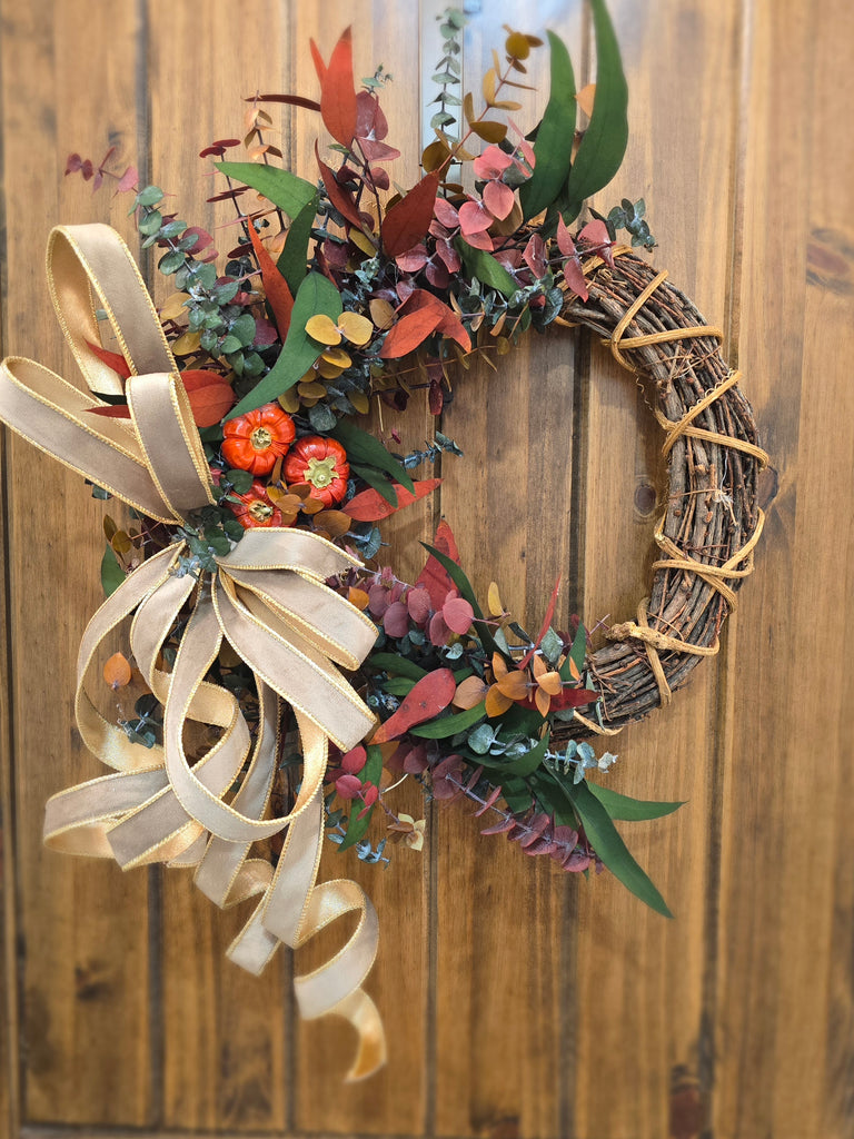 Golden Harvest Grapevine Wreath with gold velvet ribbon, preserved eucalyptus, and small orange pumpkins on a natural grapevine base.