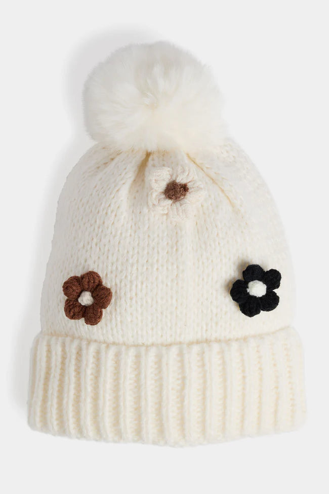 Soft knit hat with flower embellishments and fluffy pom, cozy winter accessory.