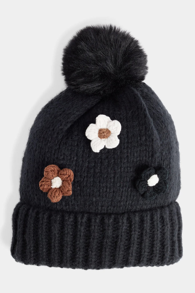 Soft knit hat with flower embellishments and fluffy pom, cozy winter accessory.