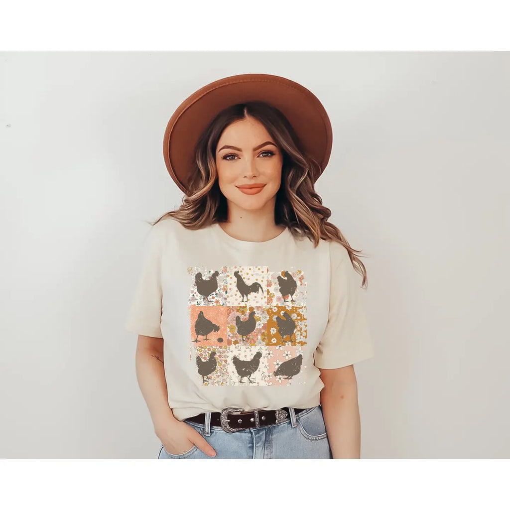 “Cream-colored graphic tee with floral patchwork squares and chicken silhouettes, modeled with jeans and a brown hat.”