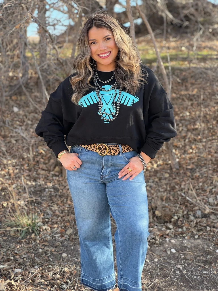 Woman wearing black waist-length sweatshirt with turquoise thunderbird graphic, 