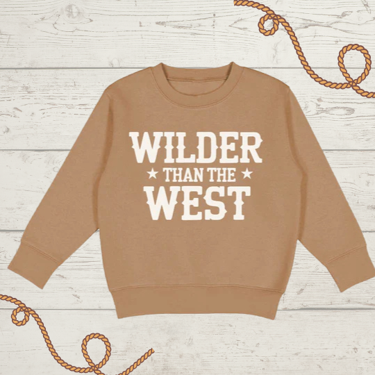 Toddler mocha sweatshirt with “Wilder Than The West” western graphic in sand print, laid flat on white wood background with rope accents